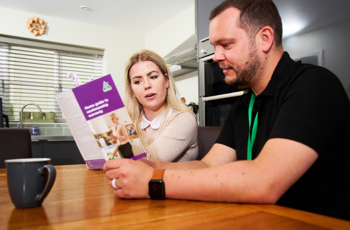 OFTEC technician showing a 'workmanship warranty' leaflet to homeowner in her kitchen 